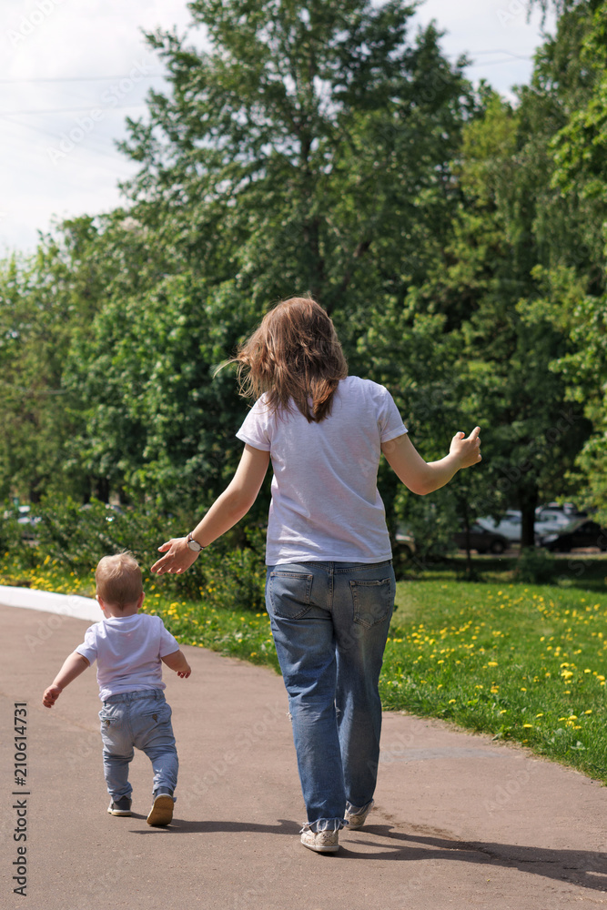 Fototapeta premium Family. Mom and son in city park. Girl and little boy are walking. Shooting from back. People are unrecognizable.