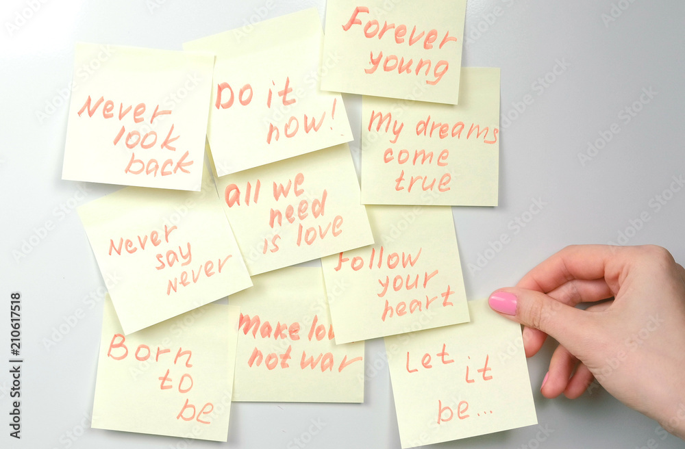 Closeup woman's hands stick yellow sticker paper sheets with motivation phrases on a white board. Closeup woman's hands stick yellow sticker paper sheets with motivation phrases on a white board.