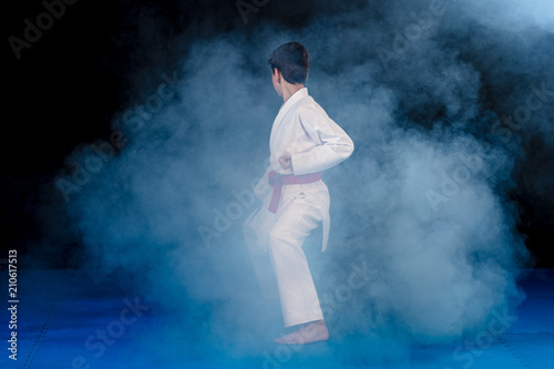 Fotografia Pre-teen boy doing karate on a black background with smoke