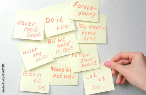 Closeup woman's hands stick yellow sticker paper sheets with motivation phrases on a white board.