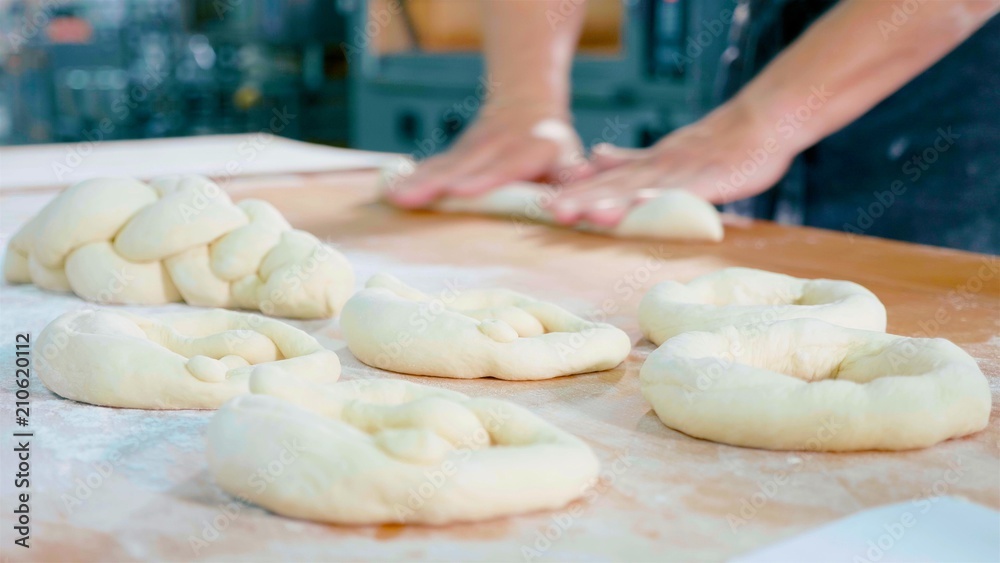 Professional baker is forming pieces of dough in bakery commercial kitchen.