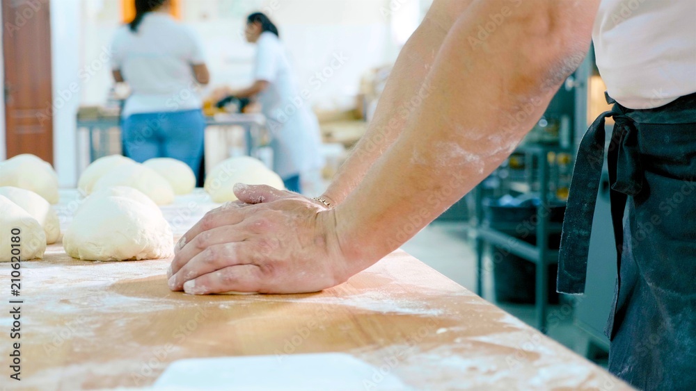 Professional baker is forming pieces of dough in bakery commercial kitchen.