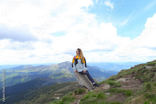 Young pretty female tourist wearing yellow jacket standing in mountains. Concept of spending summer vacations in Alps, tourism and traveling. photo