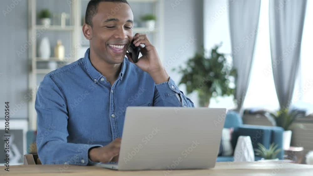 Young African Man Talking on Phone at Workplace Young African Man Talking on Phone at Workplace