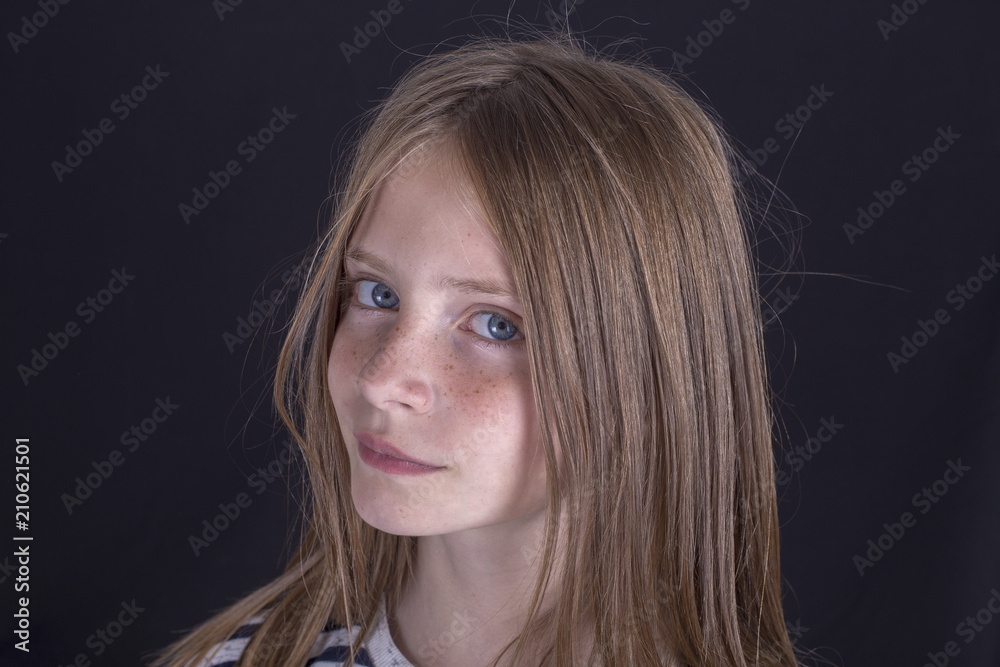 Naklejka premium Beautiful blond young girl with freckles indoors on black background, closeup portrait