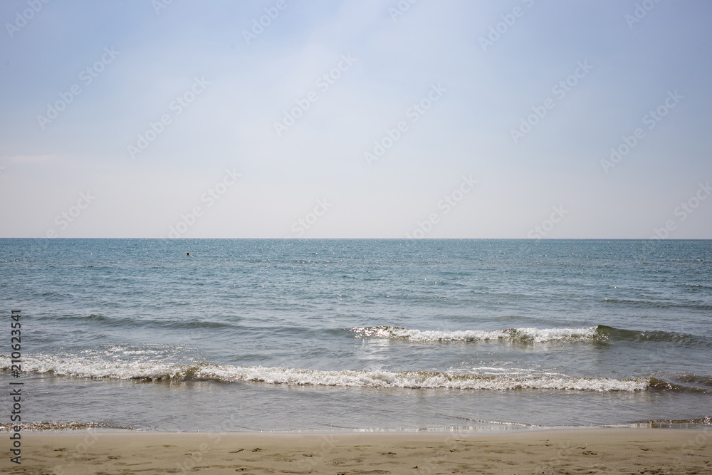 Sandy beach, sea with low waves, blue sky with few clouds for background. Close up view.