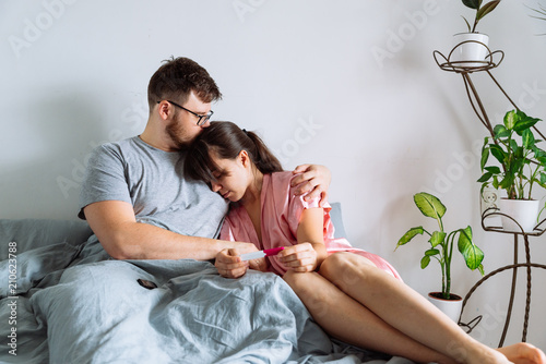 sad couple in bed looking at negative pregnancy test photo