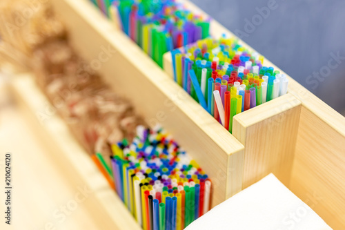 Bunch of colorful plastic sipping straws in wooden box at cafe counter. Drinks decoration and accessories. Bright multicolored background