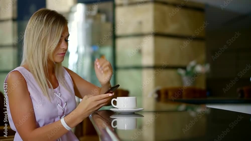 lonely woman is browsing internet in her smartphone, standing in a bar near table with cup of coffee lonely woman is browsing internet in her smartphone, standing in a bar near table with cup of coffee