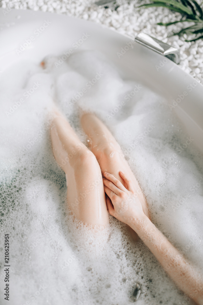 Nude legs of female person lying in bath with foam