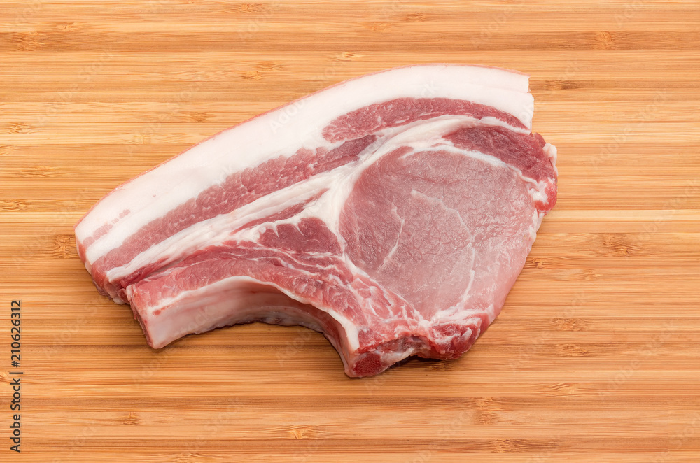 Uncooked pork loin chop bone on the bamboo cutting board Uncooked pork loin chop bone on the bamboo cutting board