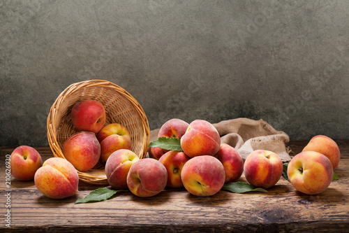 peaches with leaves in a basket on wooden table