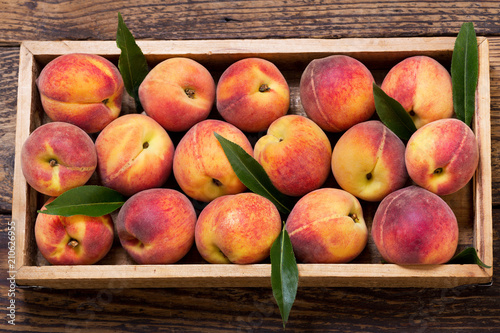 peaches with leaves in a wooden box, top view