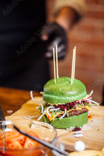 Freshly prepared green buns burger with meat cutlet, cheese, onion and paprica on wooden plate, close up photo