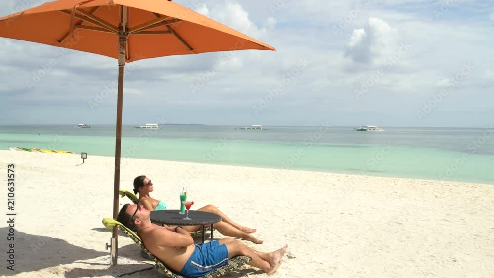A man and a woman sunbathing on sunbeds at the sea A man and a woman sunbathing on sunbeds at the sea