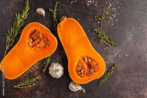 Raw cut pumpkin batternat with rosemary, thyme and garlic on a dark background, copy space.
