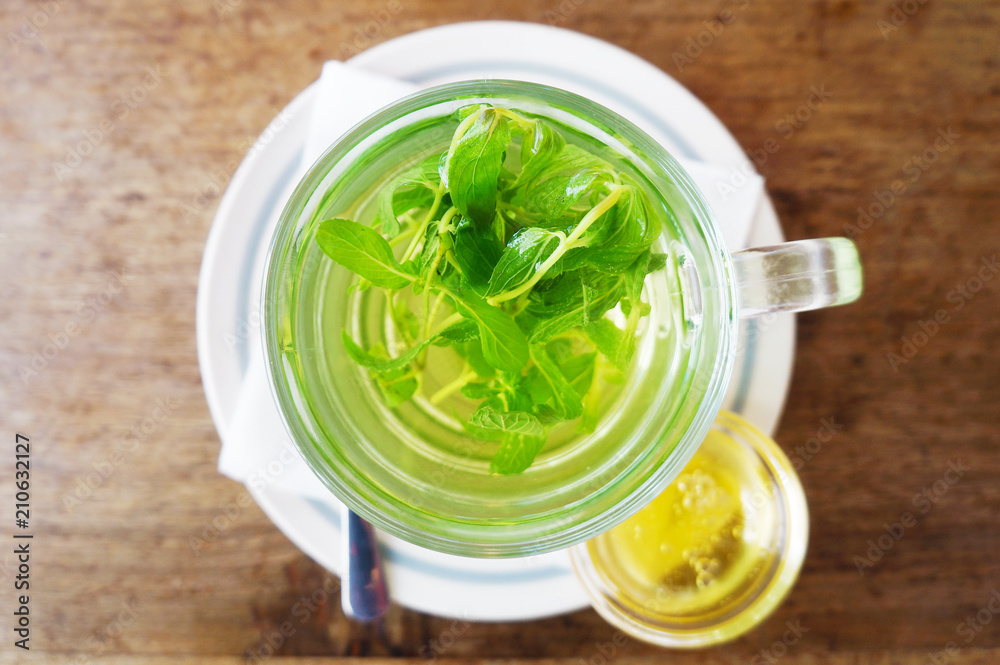 Cup of mint tea and small jar of honey on wooden table, top view Cup of mint tea and small jar of honey on wooden table, top view