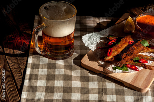 A Glass of beer, roasted breaded capelins with lemon and dip sauce on a wooden plate photo