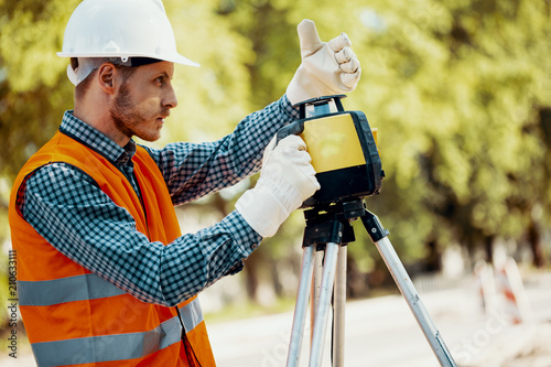 Engineer in uniform and white helmet using professional equipment during roadworks photo