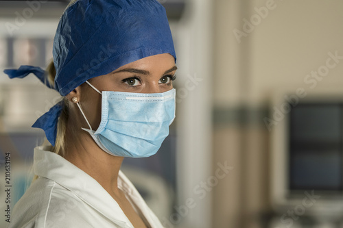 Young blonde nurse in ER room in a surgical mask and surgical cap photo