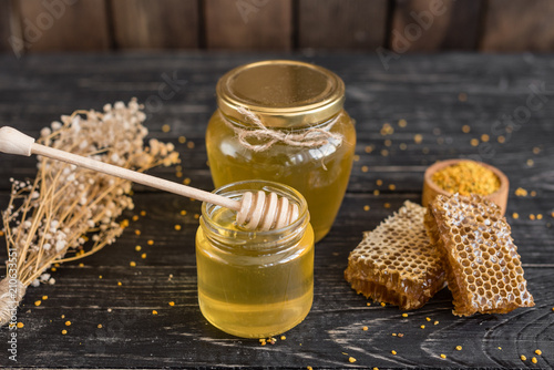 Beautiful transparent honey in bank, honeycombs and pollen on a wooden table. It can be used as a background