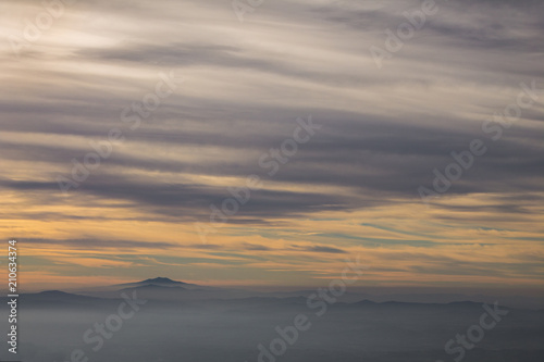 Subasio Mt. (Umbria, Italy), with sky covered by clouds and warm sunset colors, over valley filled by mist