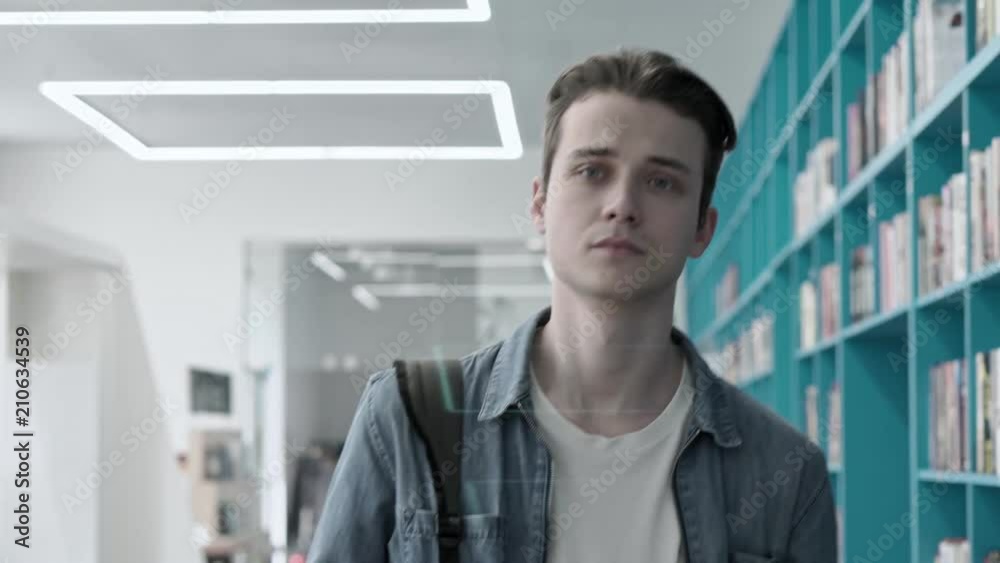 Dolly shot of handsome college student walking along book shelves in library Dolly shot of handsome college student walking along book shelves in library