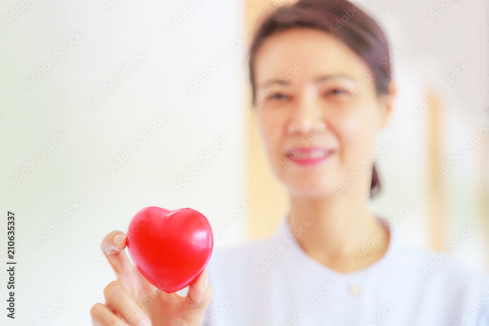 Red heart held by smiling female nurse's hand, representing giving effort high quality service mind to patient. Professional, Specialist in white uniform concept Red heart held by smiling female nurse's hand, representing giving effort high quality service mind to patient. Professional, Specialist in white uniform concept