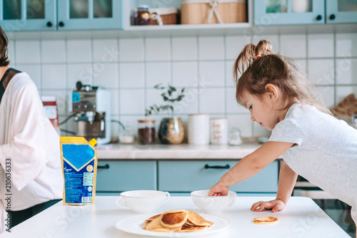 Little cute girl on kitchen is taking pancake