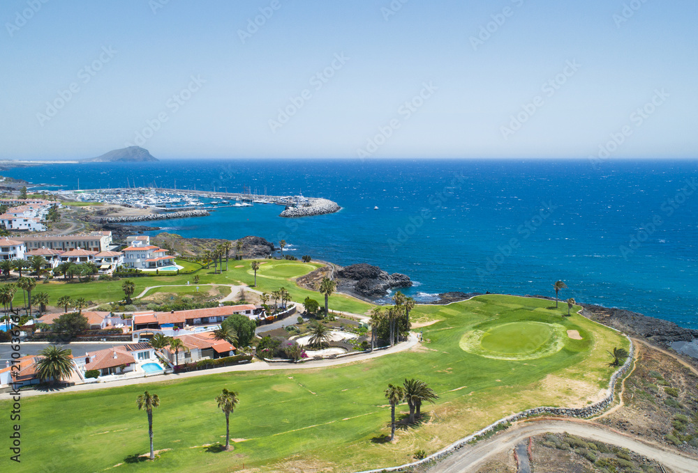Golf course and blue sea in luxurius beachfront hotel resort near atlantic ocean and yacht port. Green grass field, palm trees, house apartments, blue sky and ocean