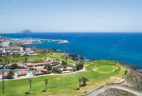 Golf course and blue sea in luxurius beachfront hotel resort near atlantic ocean and yacht port. Green grass field, palm trees, house apartments, blue sky and ocean © Space-kraft