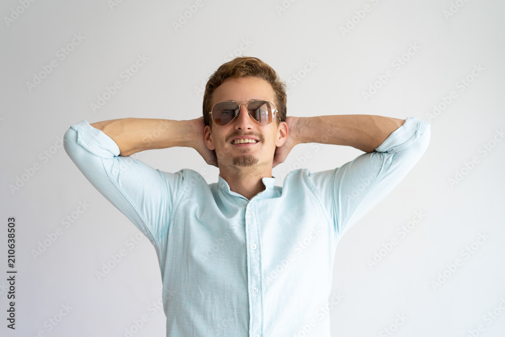 Happy peaceful guy wearing sunglasses planning vacation. Dreamy young Caucasian man keeping both hands on nap and looking up. Summer vacation and leisure concept