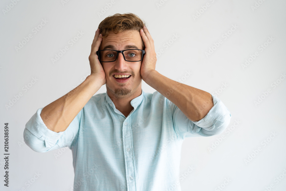 Joyful surprised guy in glasses learning great amazing news. Happy young Caucasian man in white casual shirt holding head and smiling. Great news concept Joyful surprised guy in glasses learning great amazing news. Happy young Caucasian man in white casual shirt holding head and smiling. Great news concept