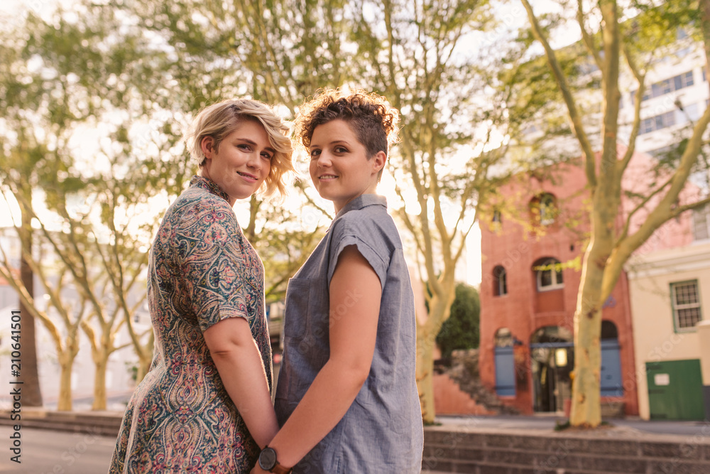 Smiling young lesbian couple holding hands on a city street
