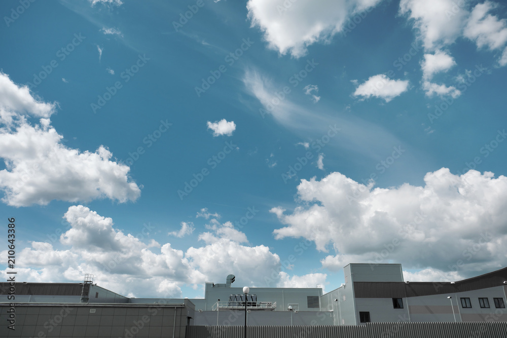 Top of the roof of a production metal building against a blue sky with clouds. Top of the roof of a production metal building against a blue sky with clouds.