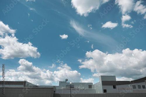 Top of the roof of a production metal building against a blue sky with clouds.