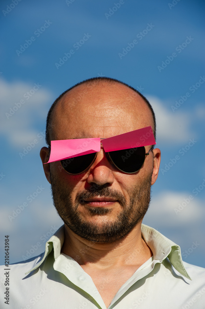 conceptual portrait of a businessman in modern sunglasses pasted with pink stickers against the blue sky. conceptual portrait of a businessman in modern sunglasses pasted with pink stickers against the blue sky.