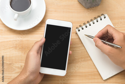 Man hand holding smart phone and pen with white blank empty screen on white desk table.Business concept.