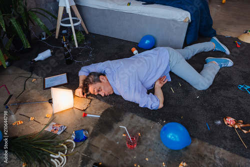 Alcohol consumption. Top view of weary mature man lying on floor and waking up