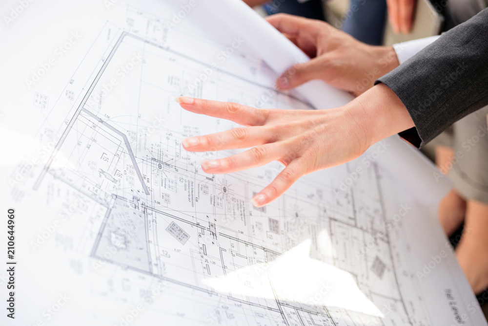 Team of successful young architects and business partners looking at blueprints and discussing during a meeting on a construction site Team of successful young architects and business partners looking at blueprints and discussing during a meeting on a construction site