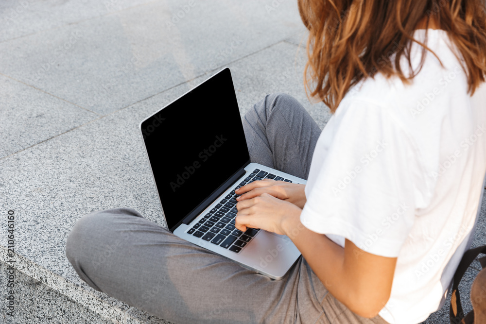 Fototapeta premium Side view of a young woman typing on laptop computer
