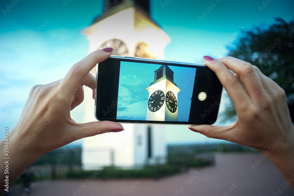Female hands holding smart phone and taking a picture of an old clock tower.