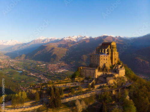 Aerial view old medieval abbey perched on mountain top, background snowy Alps at sunrise. Sacra di San Michele (italian) - Saint Michel Abbey (english traslation) - Turin, Italy