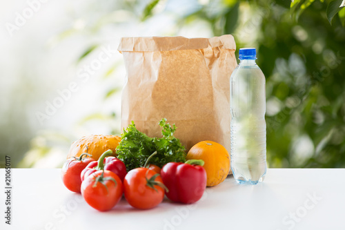 food, diet and healthy eating concept - paper bag with fresh vegetables and water bottle on table over green natural background