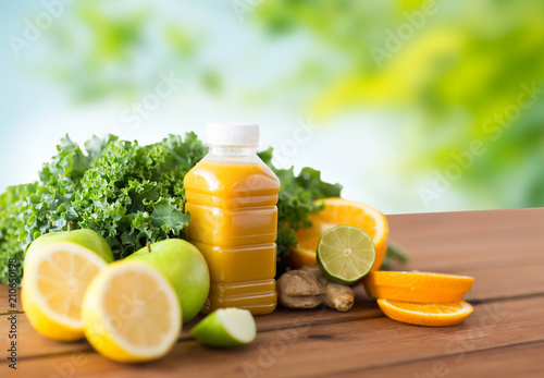 healthy eating, food, dieting and vegetarian concept - bottle with orange juice, fruits and vegetables on wooden table over green natural background
