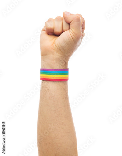 lgbt, same-sex relationships and homosexual concept - close up of male hand wearing gay pride awareness wristband showing fist