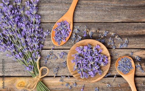 Top view of a bowl and wooden spoons with dried and fresh lavender flowers and a bouquet of lavender on a wooden background. photo