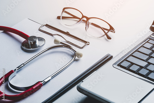 stethoscope and glasses on laptop with clipboard blank paper