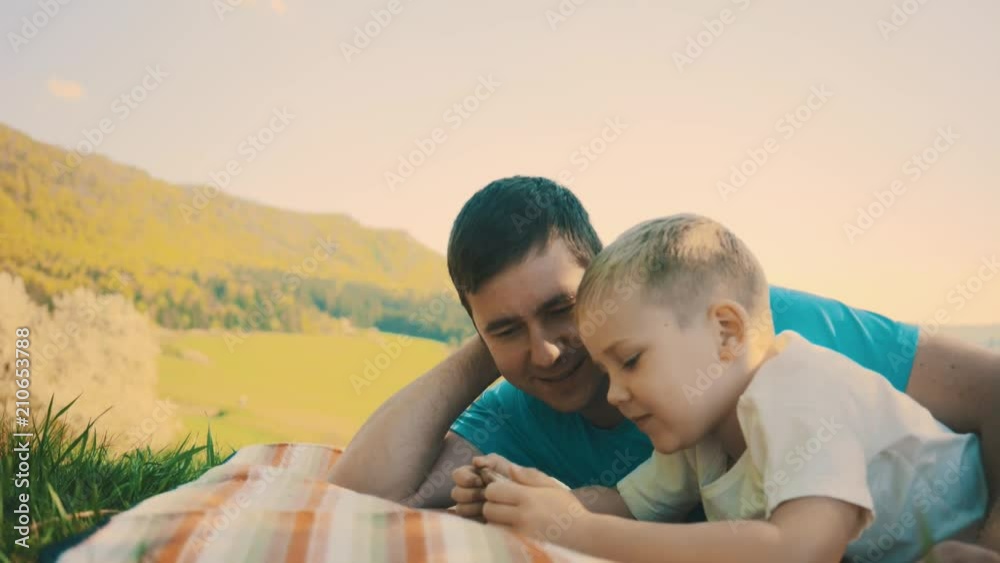 Father and son play and watching smartphone under sun light. Green field in park at sunny day mountains background
Father and son play and watching smartphone under sun light. Green field in park at sunny day mountains background
