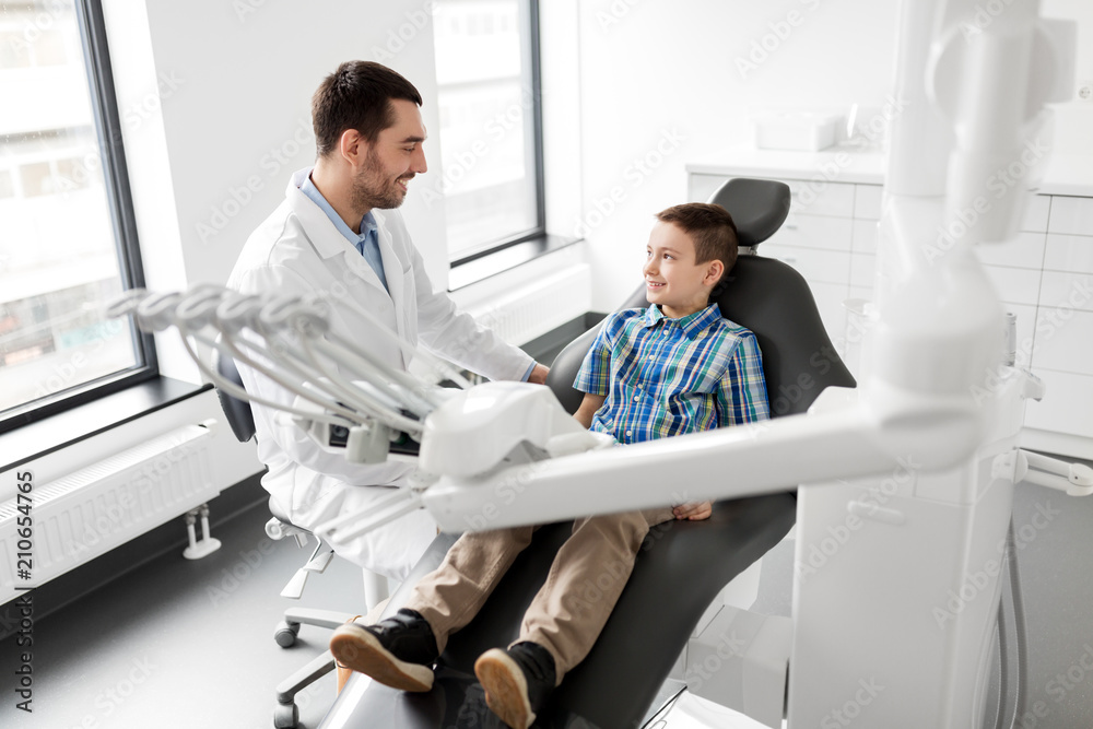 medicine, dentistry and healthcare concept - male dentist talking to kid patient at dental clinic